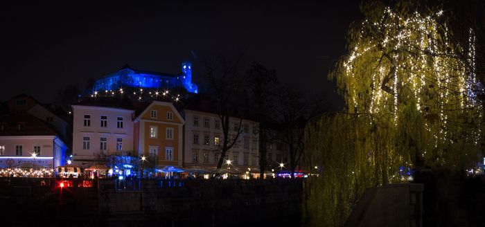 Ljubljana Castle lit in blue above the stalls by the river.