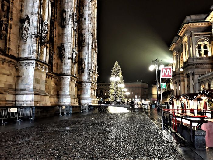 The chalets along the flank of the Duomo with the tree at the far end of the square, on a rainy night (photographed in 2017).