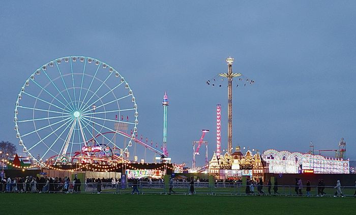 The wheel, the carousel and the lit arches at dusk, photographed in 2025.